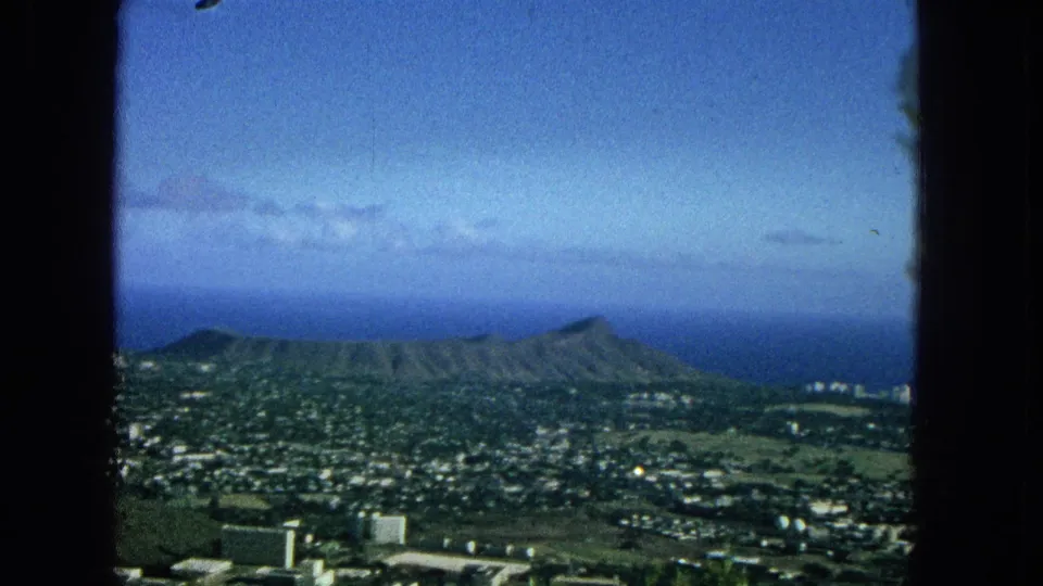 Metadata-supported 1965 view of Diamond Head and Honolulu, with mid-century buildings and neighborhoods below a blue Pacific horizon, partially bordered by a window frame.
