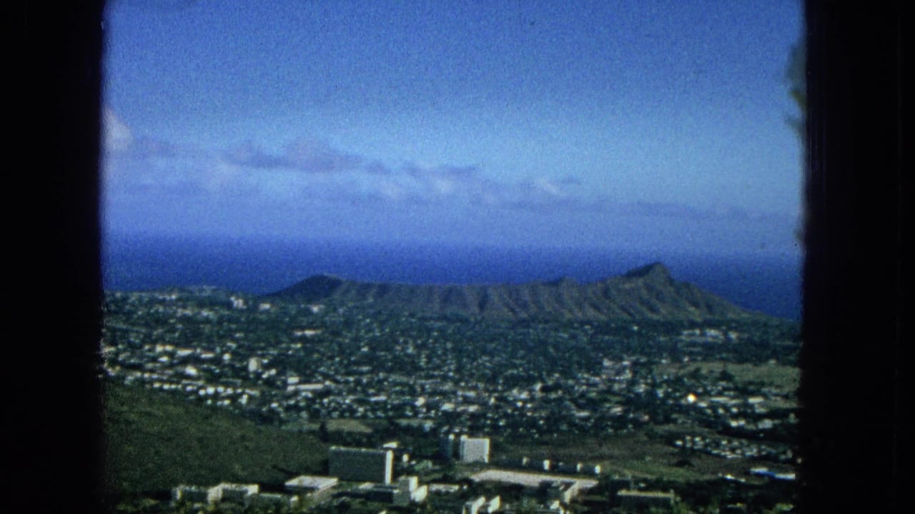 1965 Oahu view from an elevated position, with Diamond Head, Honolulu-area buildings, green terrain, ocean horizon, clouds, and dark window framing visible.