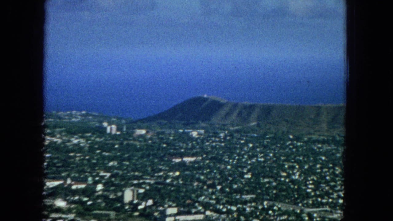1965 Honolulu cityscape seen from an elevated or aerial viewpoint, with Diamond Head crater rising behind dense neighborhoods and the Pacific Ocean in the distance.
