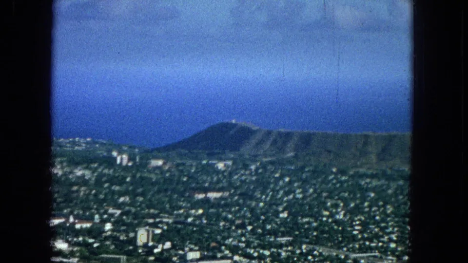 Elevated or aerial 1965 view across Honolulu toward Diamond Head, with urban blocks in the foreground and ocean visible beyond the crater.