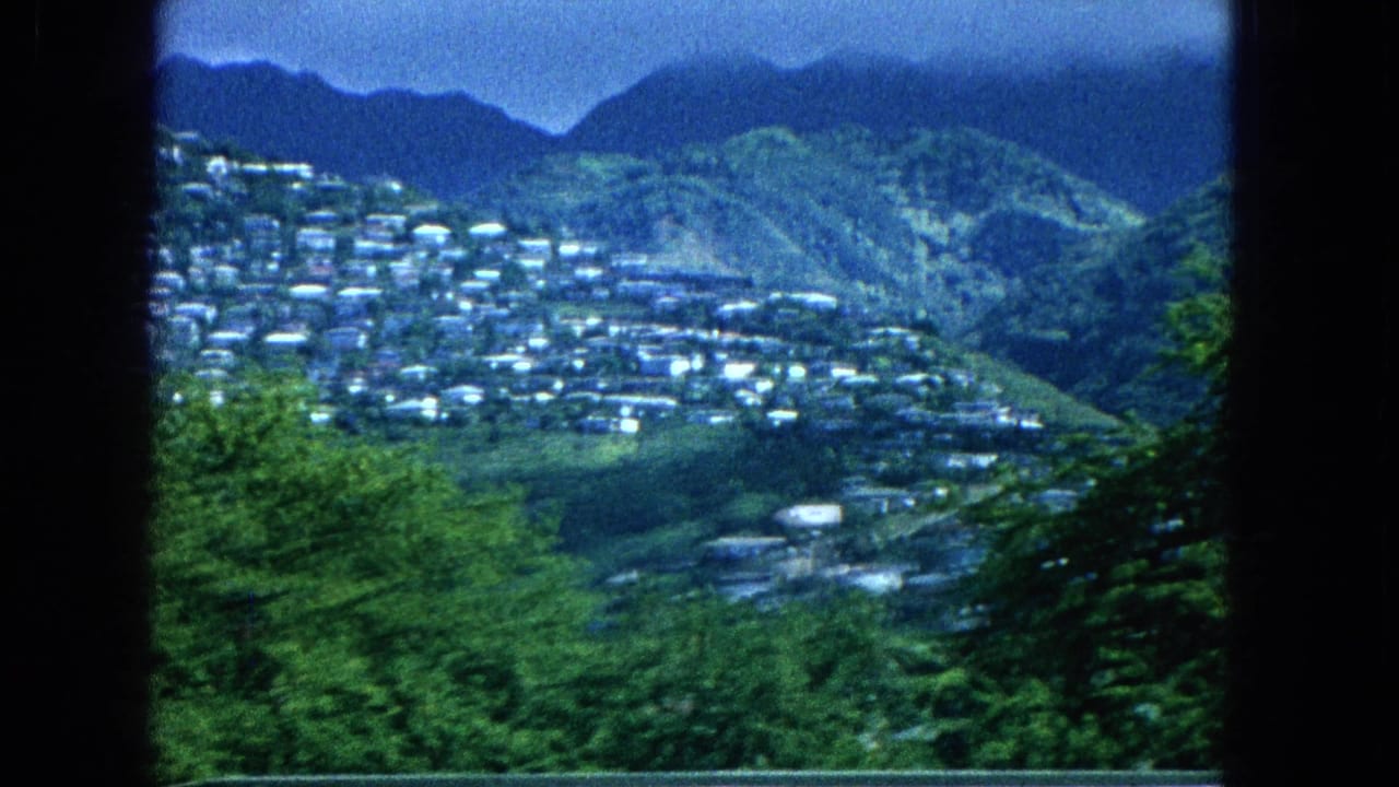 Distant settlement spread across a green hillside with mountains behind it.