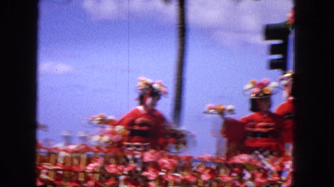 Parade performers in red outfits pass on a decorated float beside a traffic signal.