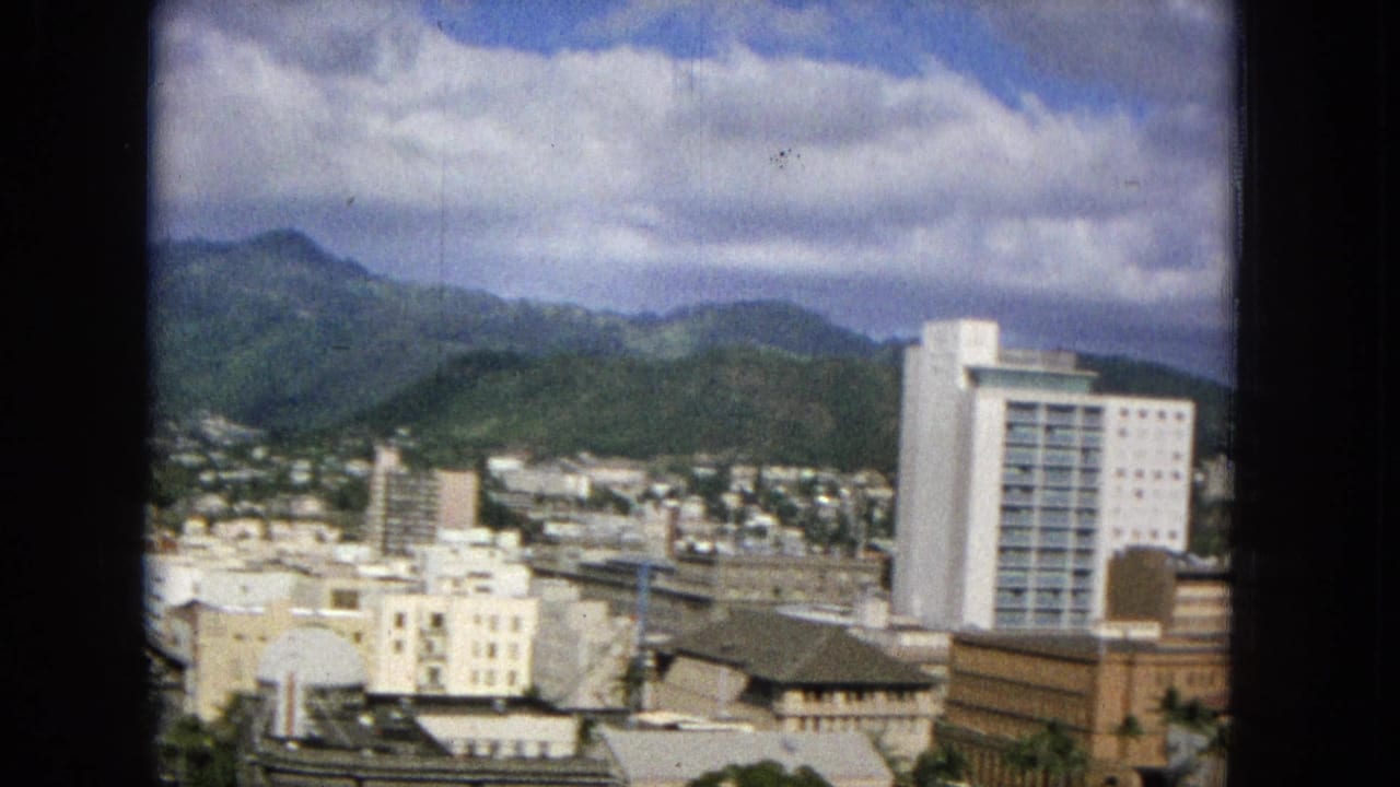 City buildings and a white tower set below green mountain ridges.