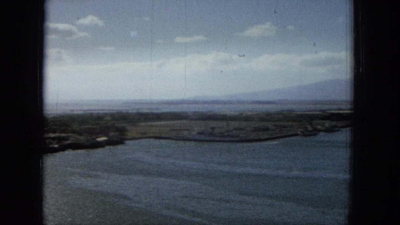 Wide coastal water view with shoreline and distant mountains beyond a window frame.