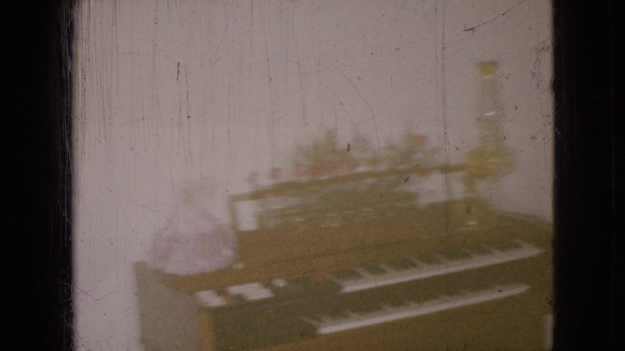 Soft 8mm interior view of an upright piano with a yellow lamp and floral arrangement in a private Wellsburg, Iowa home.