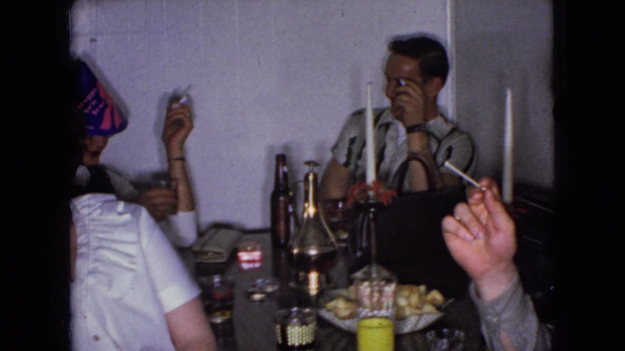 In 1965 Wellsburg, Iowa home-movie footage, adults gather at a private table with candles, bottles, glasses, cigarettes, and small party hats visible.
