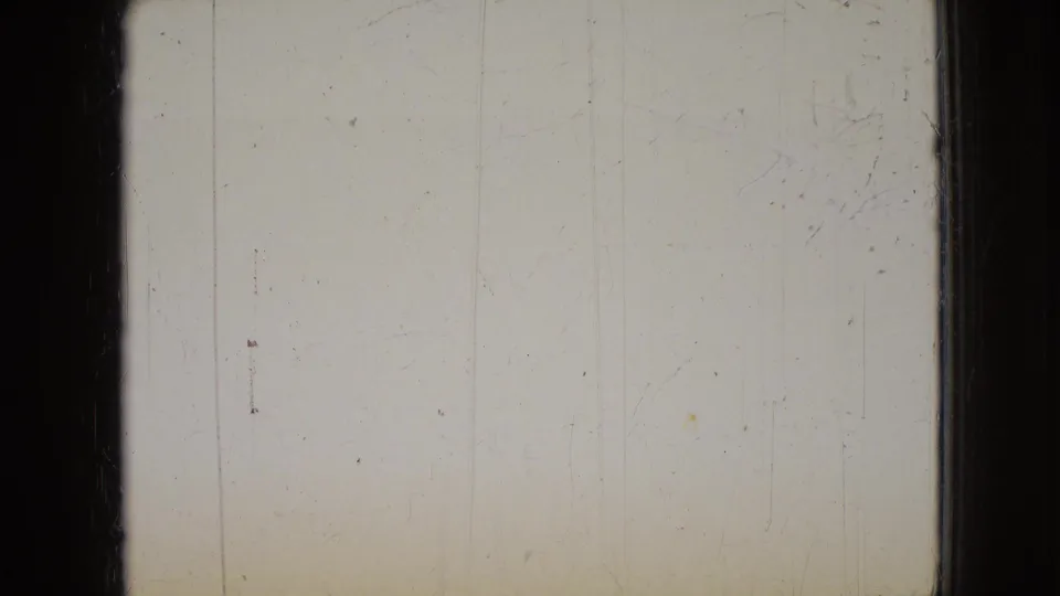 A mostly blank or overexposed 8mm frame with dark film borders, faint vertical marks, and visible surface wear before the living-room action appears.
