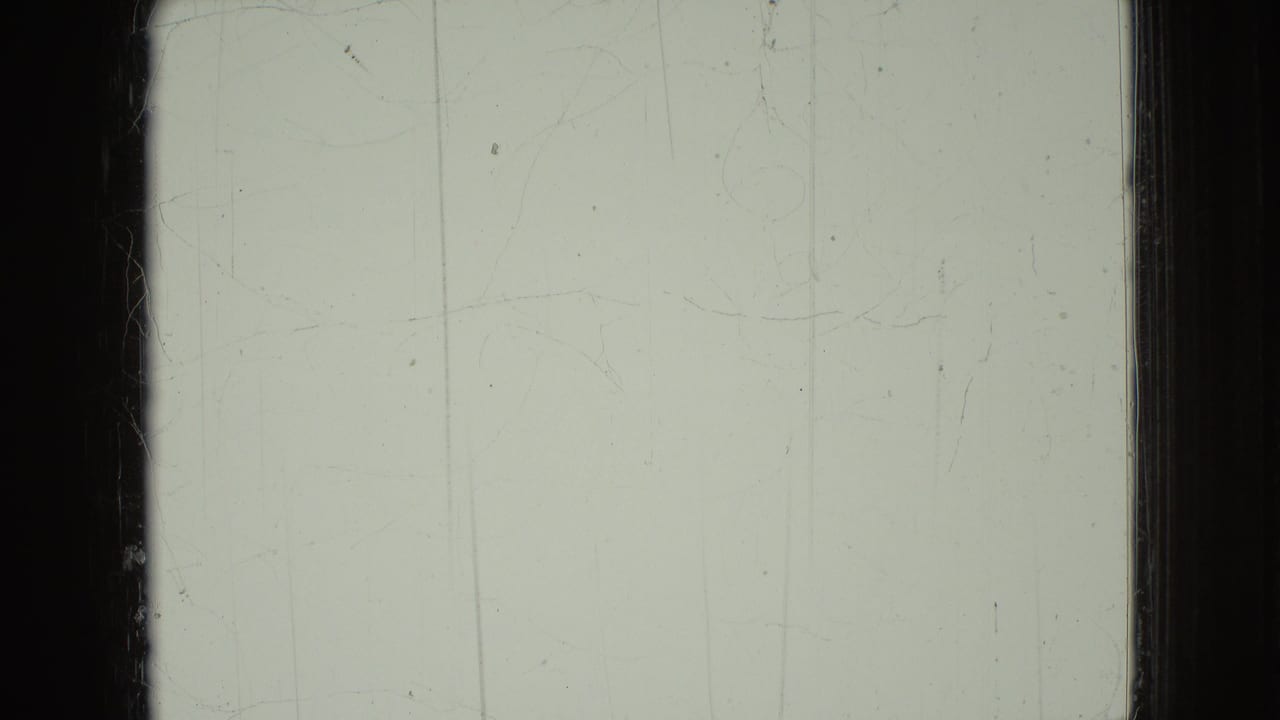 A pale, overexposed 8mm frame with visible scratches, dust, and dark frame borders, likely from the same Wellsburg, Iowa home-movie reel.