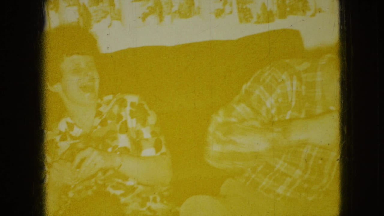 Adults on a couch, including a laughing woman and a man in a plaid shirt, seen through yellowed film exposure.
