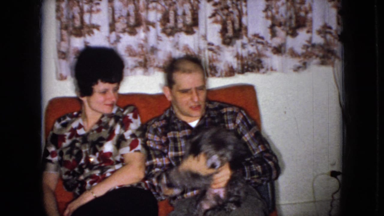 Man holds a small shaggy dog while a woman sits beside him on a red couch.
