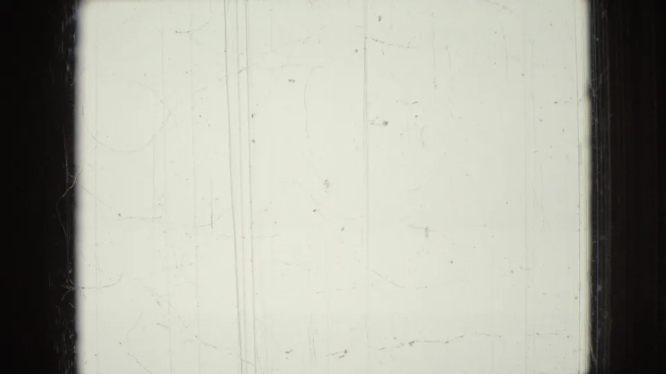Pale 8mm frame with visible scratches, dust marks, and dark vertical film borders, with no clear subject visible.