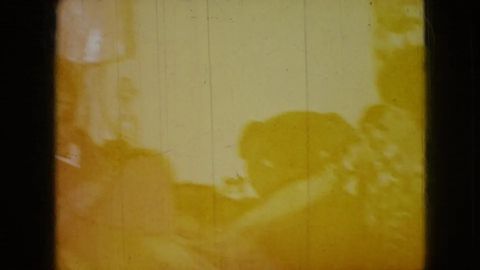 Yellow-tinted Wellsburg, Iowa 8mm frame showing seated figures in a private living-room interior with a dog low in the frame.