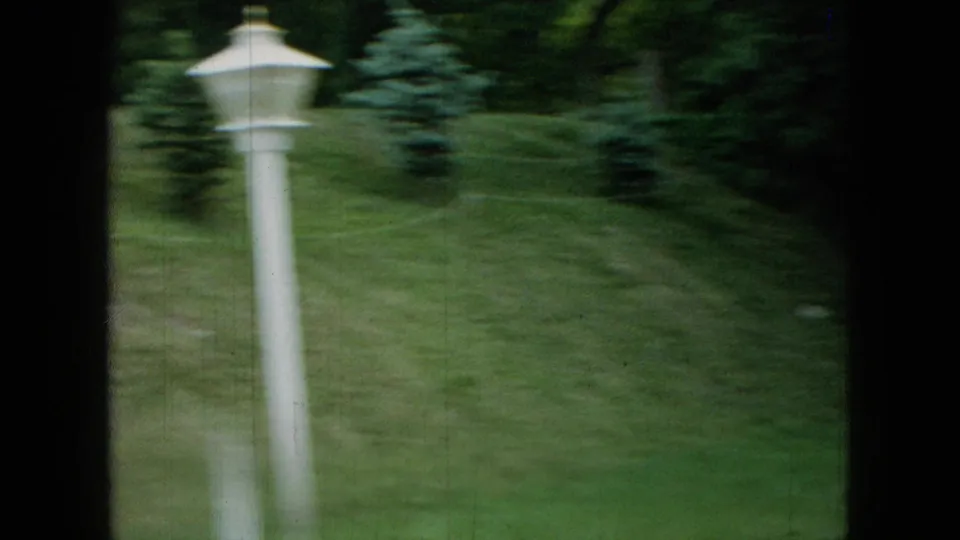 The final frame shows the residential lawn after the girl has moved out of view, with a white yard lamp, shrubs, trees, and soft 8mm exposure.