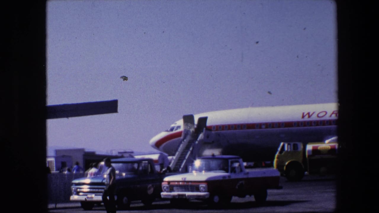 Parked World Airways aircraft with stairs, two pickup trucks, and people crossing the tarmac.