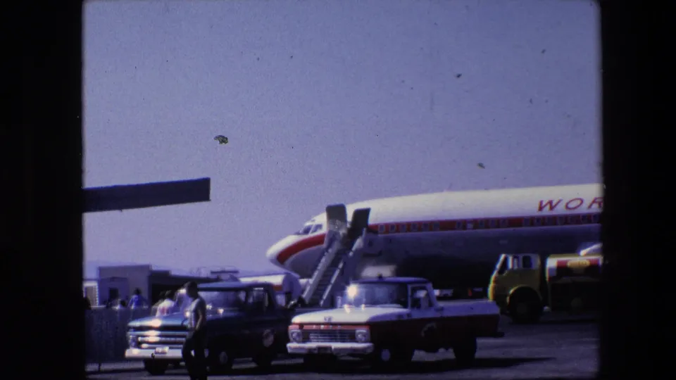The aircraft remains parked on the ramp as people walk between pickup trucks and mobile stairs, with the World Airways name partly visible on the fuselage.