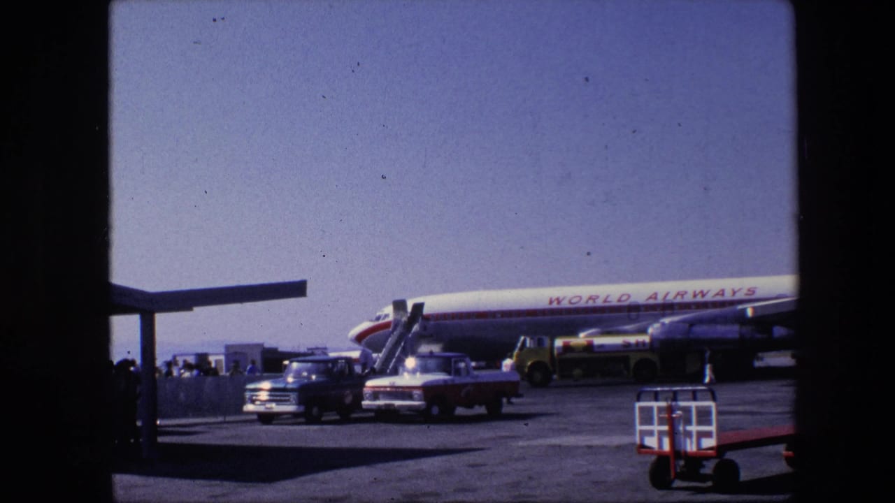 Parked World Airways airliner with stairs, vehicles, baggage cart and people on the tarmac.