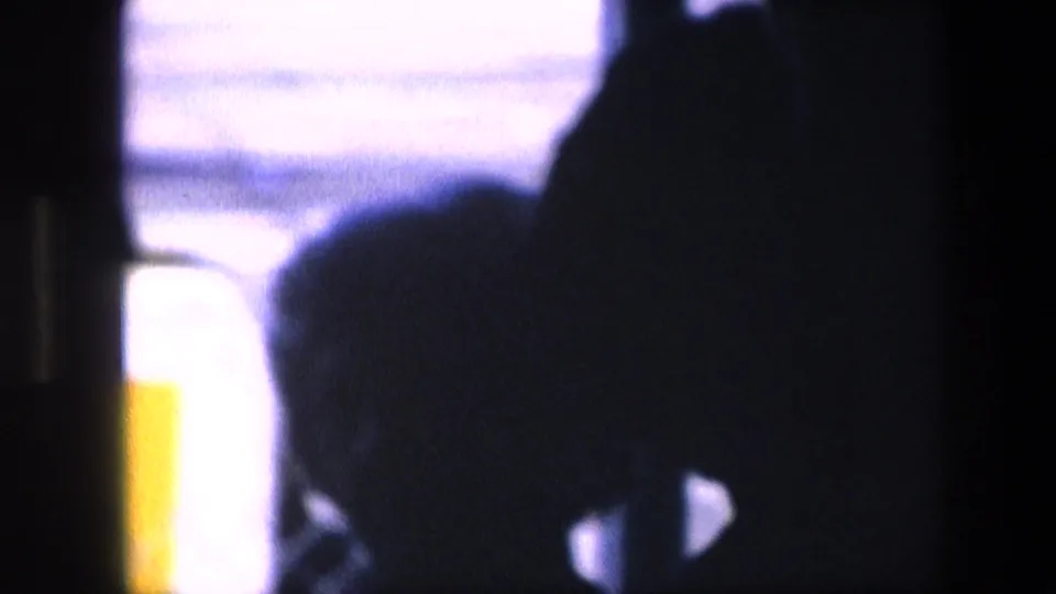 Blurry 8mm frame with dark passenger-like silhouettes against bright airport or aircraft-window light, continuing the travel-home-movie viewpoint.