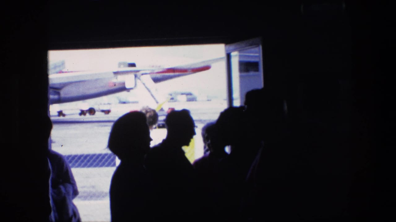 1967 home-movie airport scene with passengers in silhouette near a bright doorway and an aircraft visible on the tarmac.