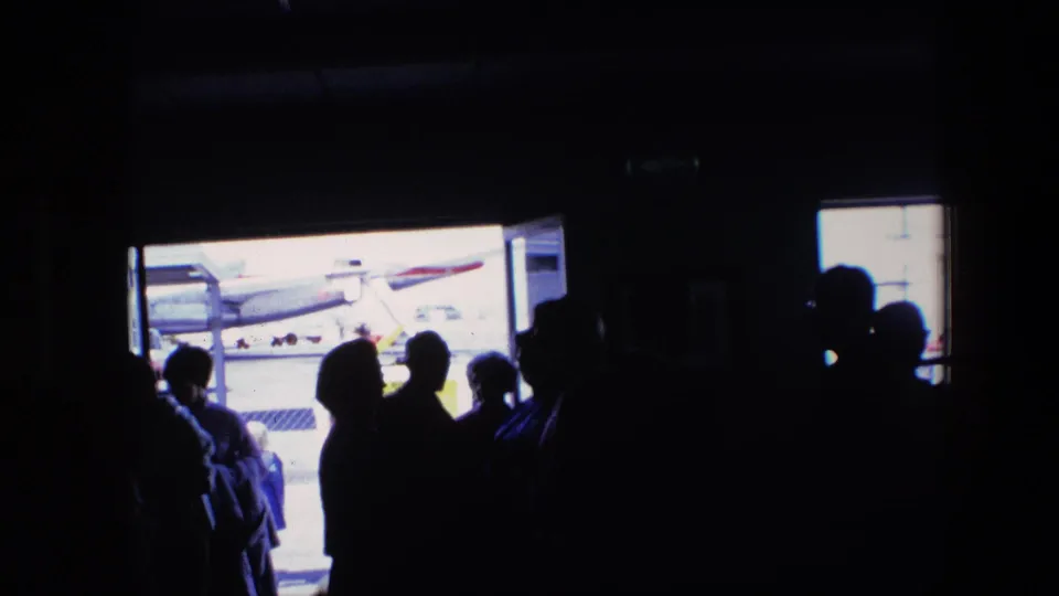 A short 1960s airport travel moment shows silhouetted passengers inside a dark space looking toward the aircraft and daylight outside.