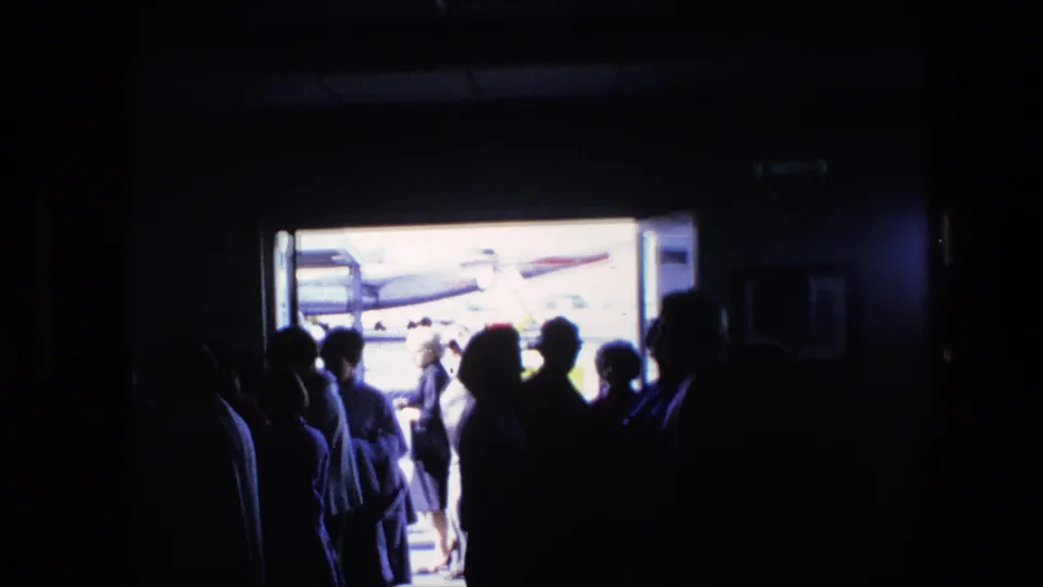 A queue-like group of travelers is seen from inside a dim airport area, with the bright exterior and aircraft details beyond the opening.