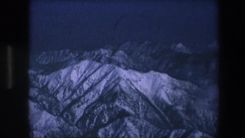 Grainy 8mm frame showing snowy mountain peaks in blue twilight, likely a scenic insert or projected-looking view within the same short clip.