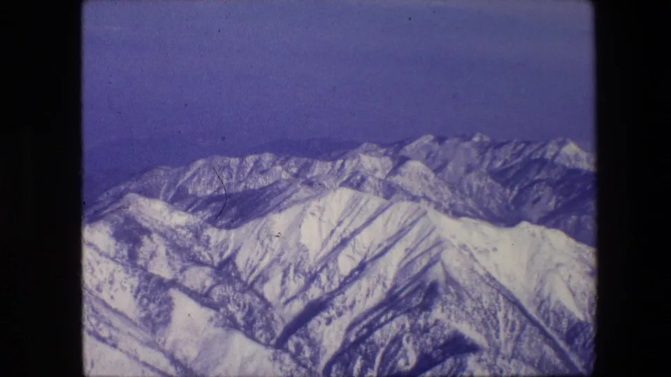 1967 small-gauge film frame of snow-covered slopes and a distant ridgeline, with soft focus, grain, and purple-blue color cast.