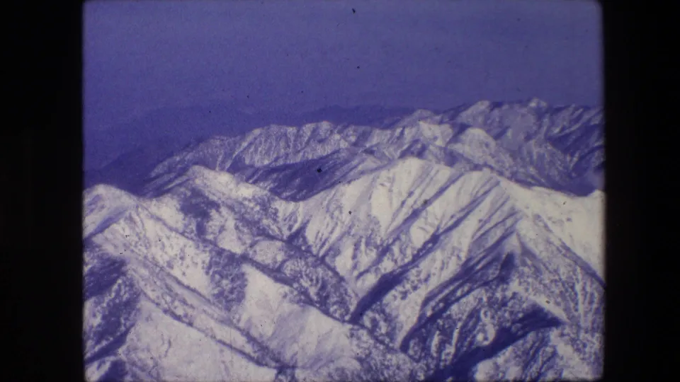 Final sampled frame showing a snowy mountain range with dark valley lines, blue sky, visible grain, dust, and aged 8mm film coloration.