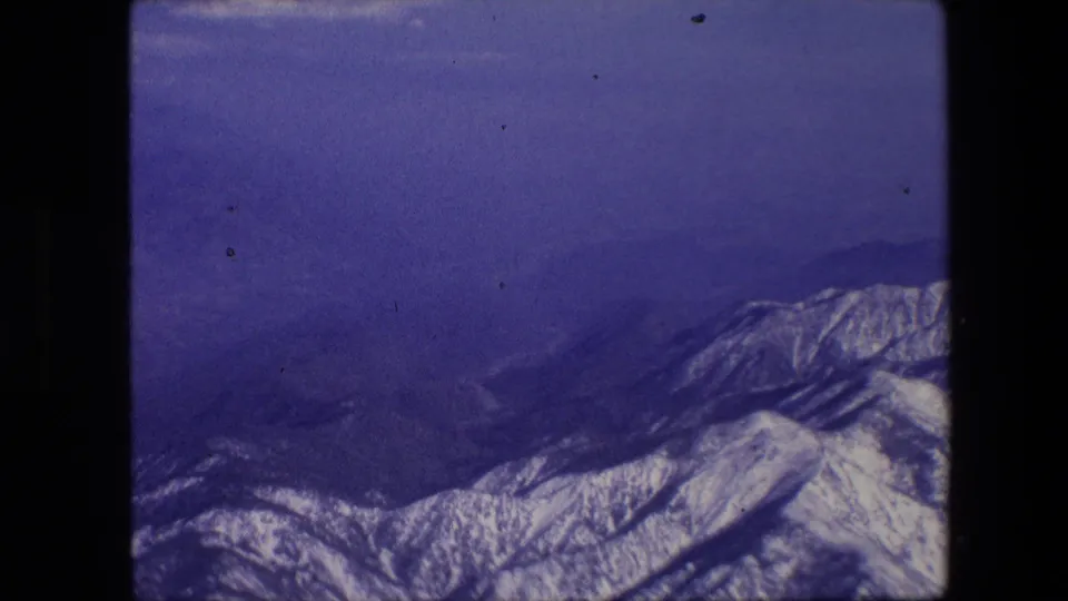 1967 8mm aerial view with snow-covered ridges low in the frame and broad blue sky or atmospheric haze above.
