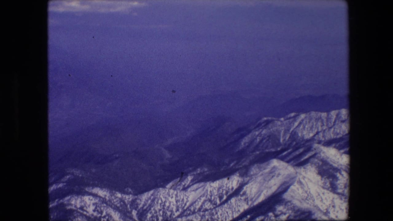 Snow-covered mountain ridges appear under a blue-purple sky in 1967 8mm home-movie footage from an aircraft passenger viewpoint.