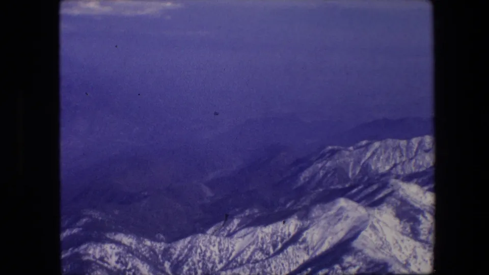 Snow-covered mountain ridges appear under a blue-purple sky in 1967 8mm home-movie footage from an aircraft passenger viewpoint.