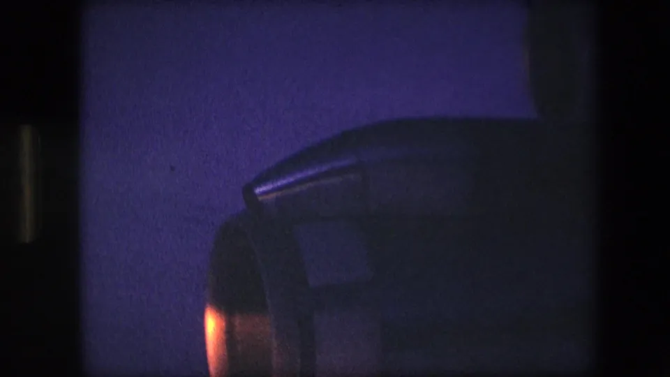 A large aircraft engine housing fills the frame in blue night exposure, with warm orange light along the lower left and visible 8mm film texture.