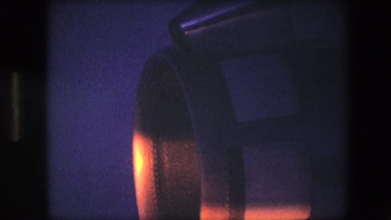 1967 archival 8mm frame showing a close view of a turbine-like aircraft component under orange light against a blue-purple low-light background.