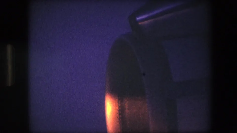 1960s 8mm frame showing a close, soft-focus view of turbine-like machinery with a bright orange glow and visible film grain.