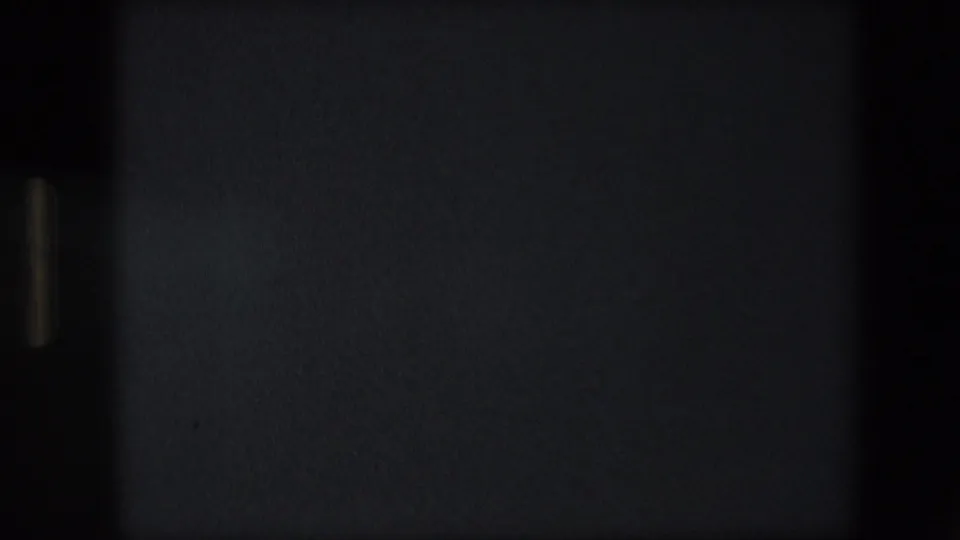 End frame from the 8mm clip, mostly dark with faint film grain and minimal visible detail from the machinery scene.