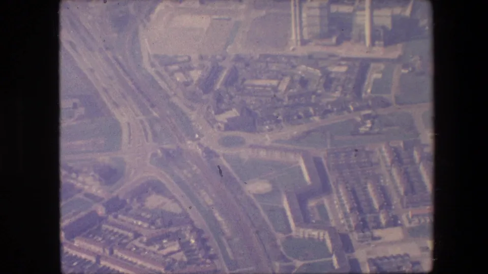 Faded 8mm aerial frame showing intersecting roads, urban blocks, and industrial or commercial-looking structures from an aircraft.