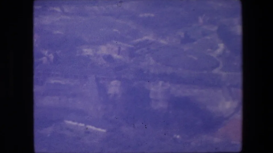 Soft 1967 8mm aerial view with indistinct ground features, visible film wear, and a strong blue-purple color cast.