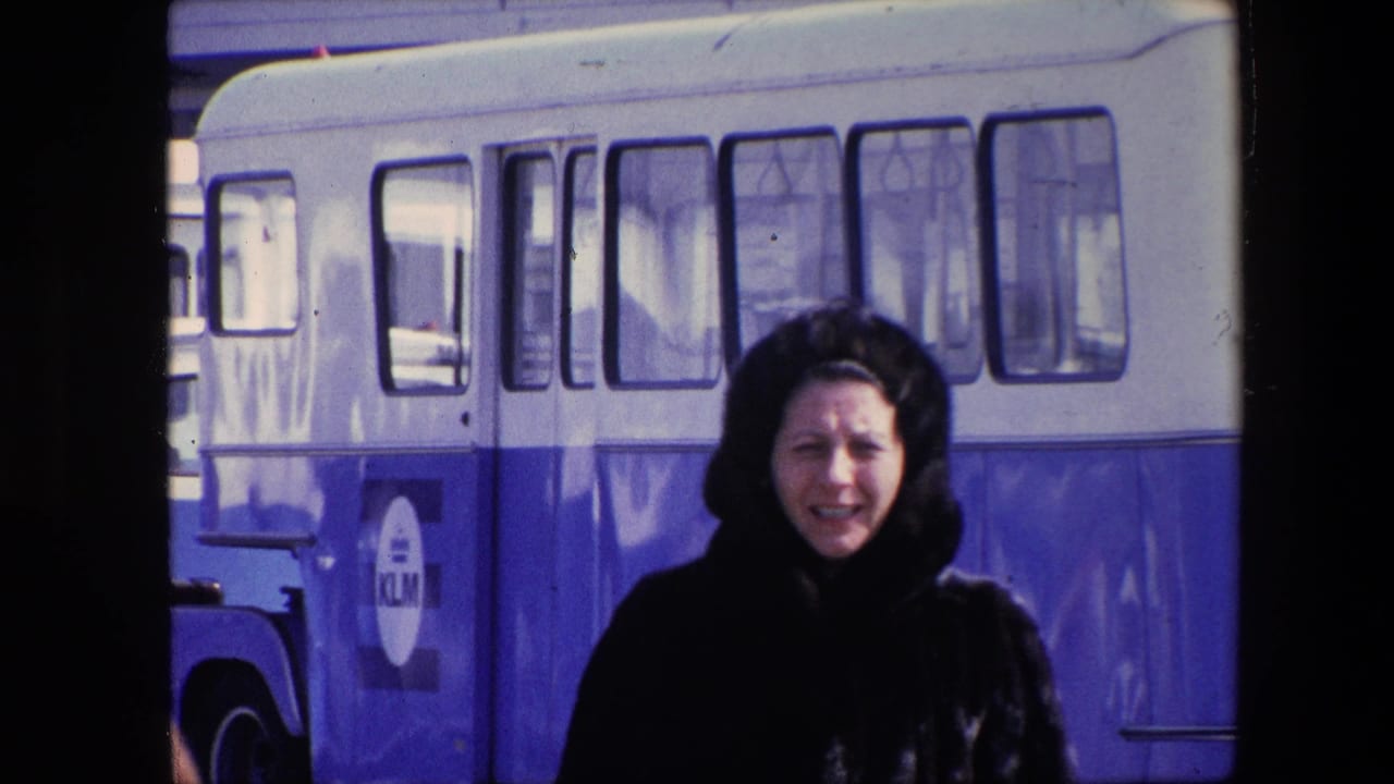 The woman turns toward the camera with the KLM-marked bus filling the background in a soft, blue-shifted 8mm street frame.