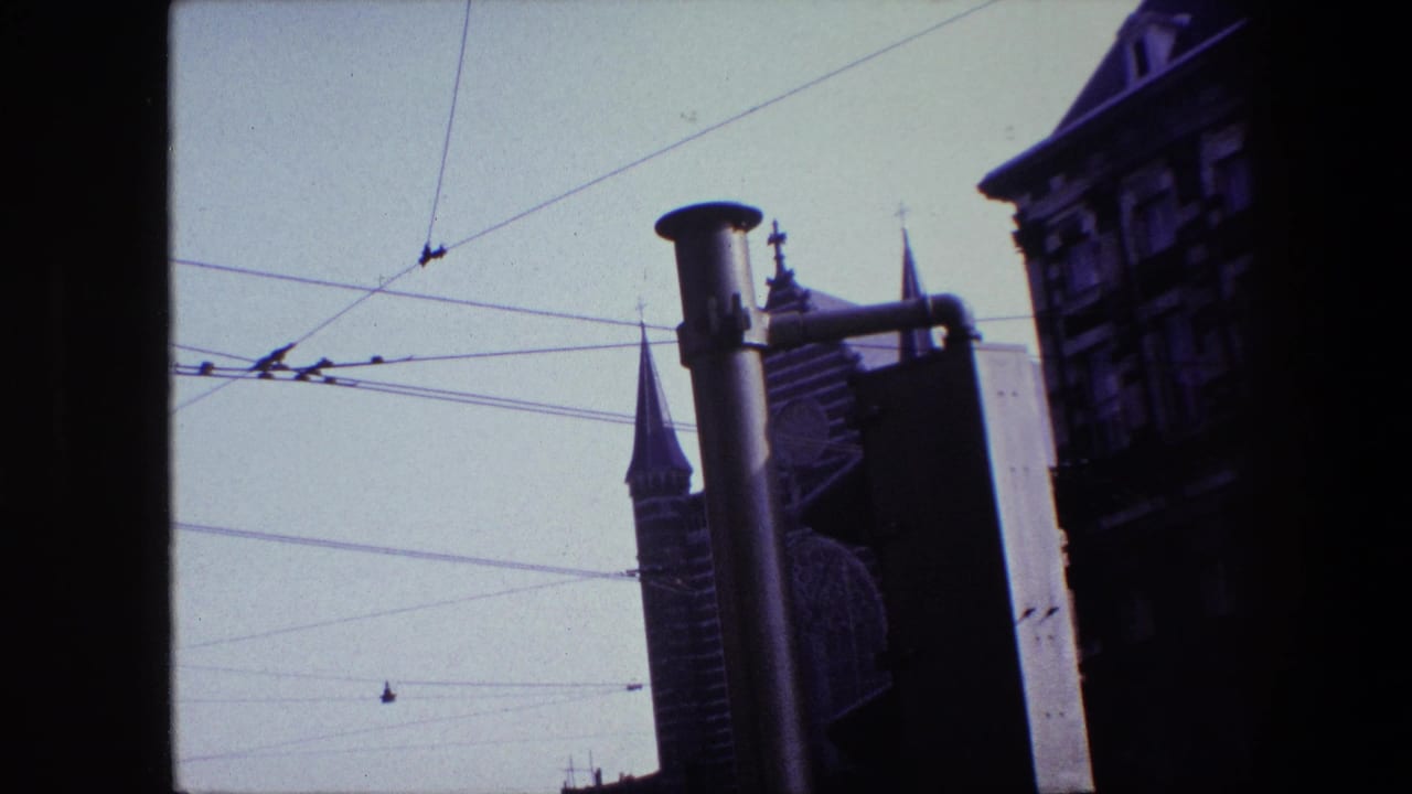 1967 Amsterdam frame with tram or trolley wires crossing a pale sky above pointed church towers and a dark architectural facade at right.