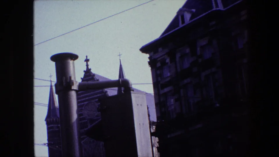 1967 Amsterdam frame showing a church spire with cross, a shadowed multi-story facade, and overhead transit wires from a tilted vehicle-shot angle.