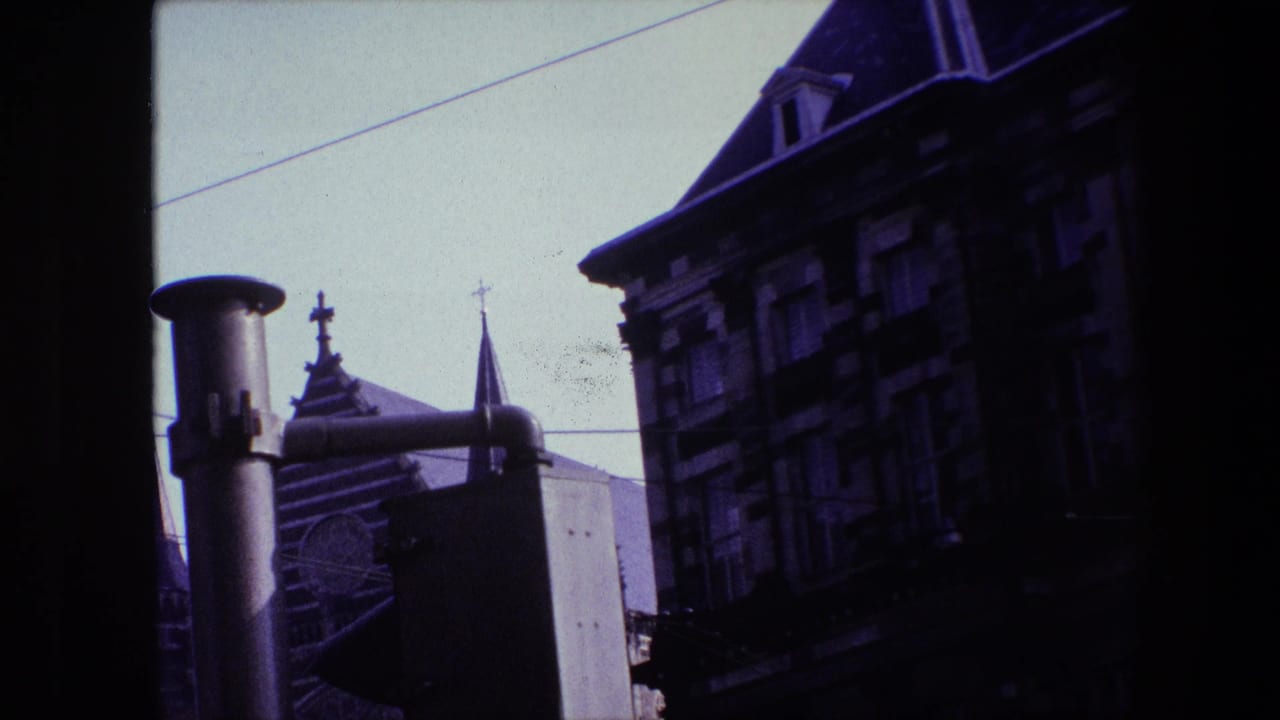 1967 Amsterdam home-movie frame showing old buildings and church spires with crosses seen through a dark window frame under a pale sky.