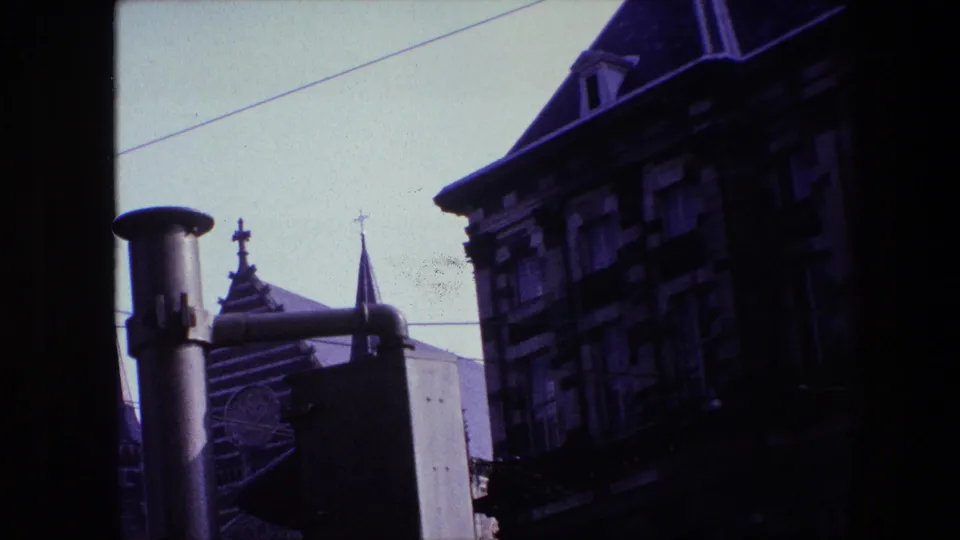 1967 Amsterdam home-movie frame showing old buildings and church spires with crosses seen through a dark window frame under a pale sky.