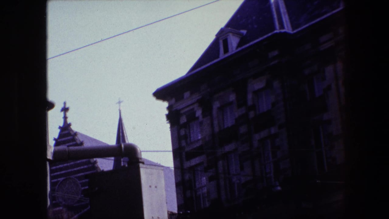 1967 Amsterdam frame with a dark vertical window divider separating views of a church spire, crosses, steep roofs, and old facade details.