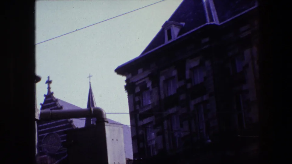 1967 Amsterdam frame with a dark vertical window divider separating views of a church spire, crosses, steep roofs, and old facade details.