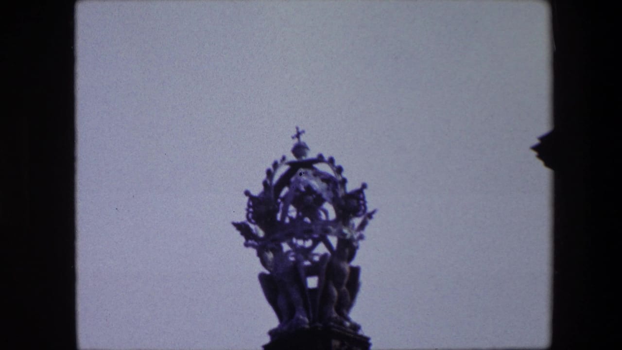 1967 Amsterdam home-movie frame showing an ornate church steeple and cross silhouetted against a pale sky with dark edge framing.