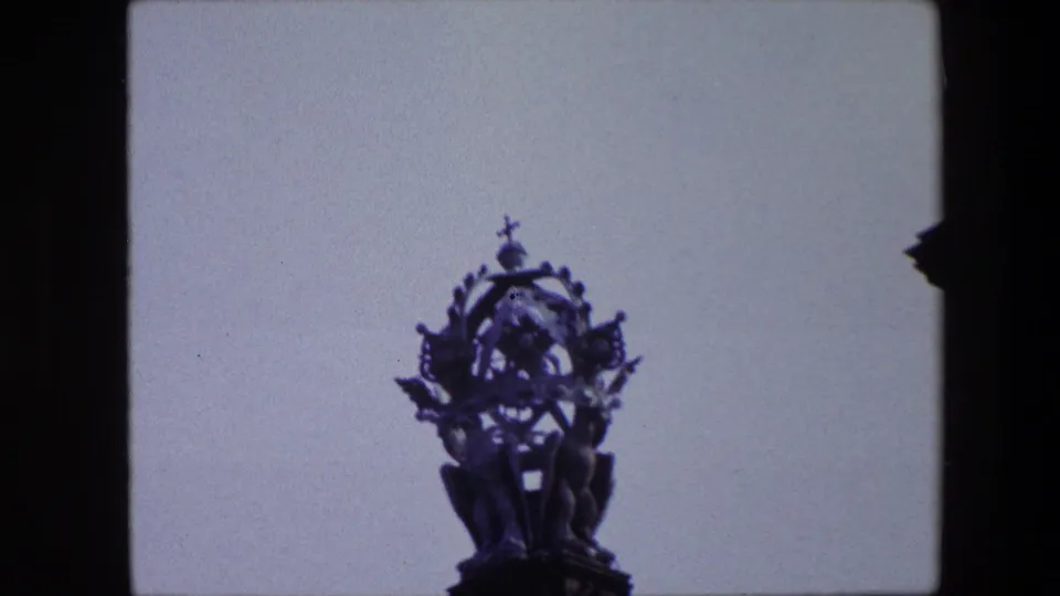 1967 Amsterdam home-movie frame showing an ornate church steeple and cross silhouetted against a pale sky with dark edge framing.