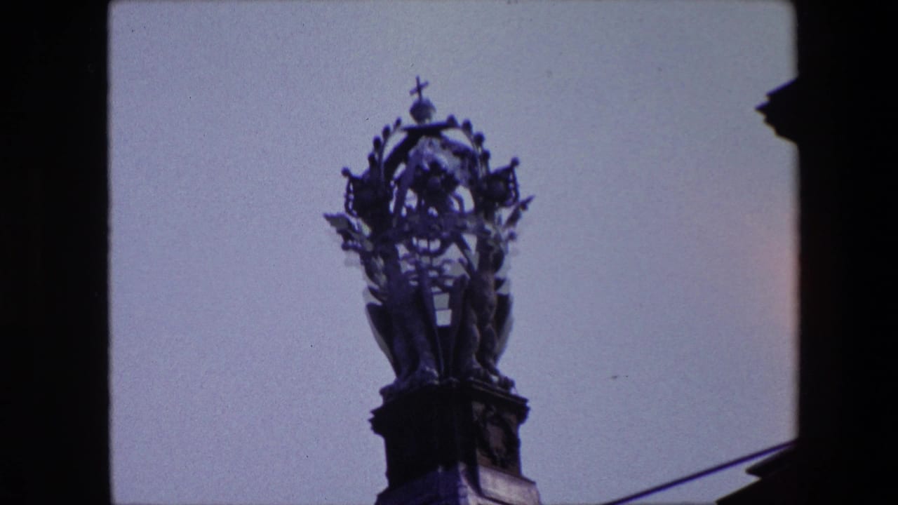 Closer 1967 Amsterdam view of the church spire, cross, and sculptural roof detail, with the frame partly bordered by a dark building edge.