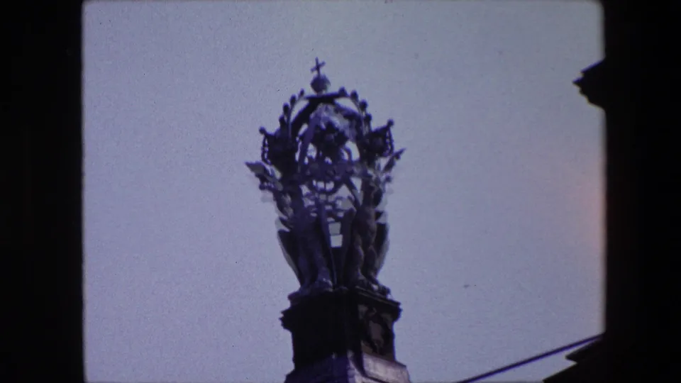 Closer 1967 Amsterdam view of the church spire, cross, and sculptural roof detail, with the frame partly bordered by a dark building edge.