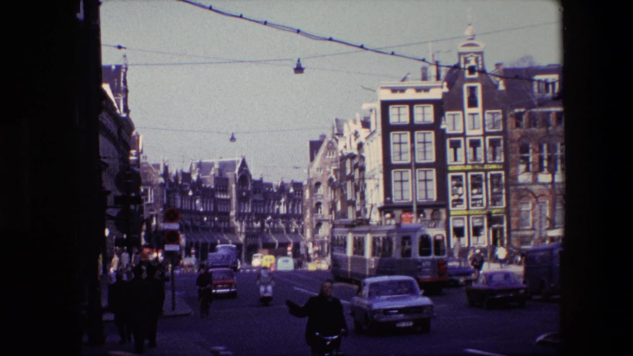 1967 Amsterdam street view with an electric tram, period cars, overhead wires, pedestrians, and tall historic building facades.