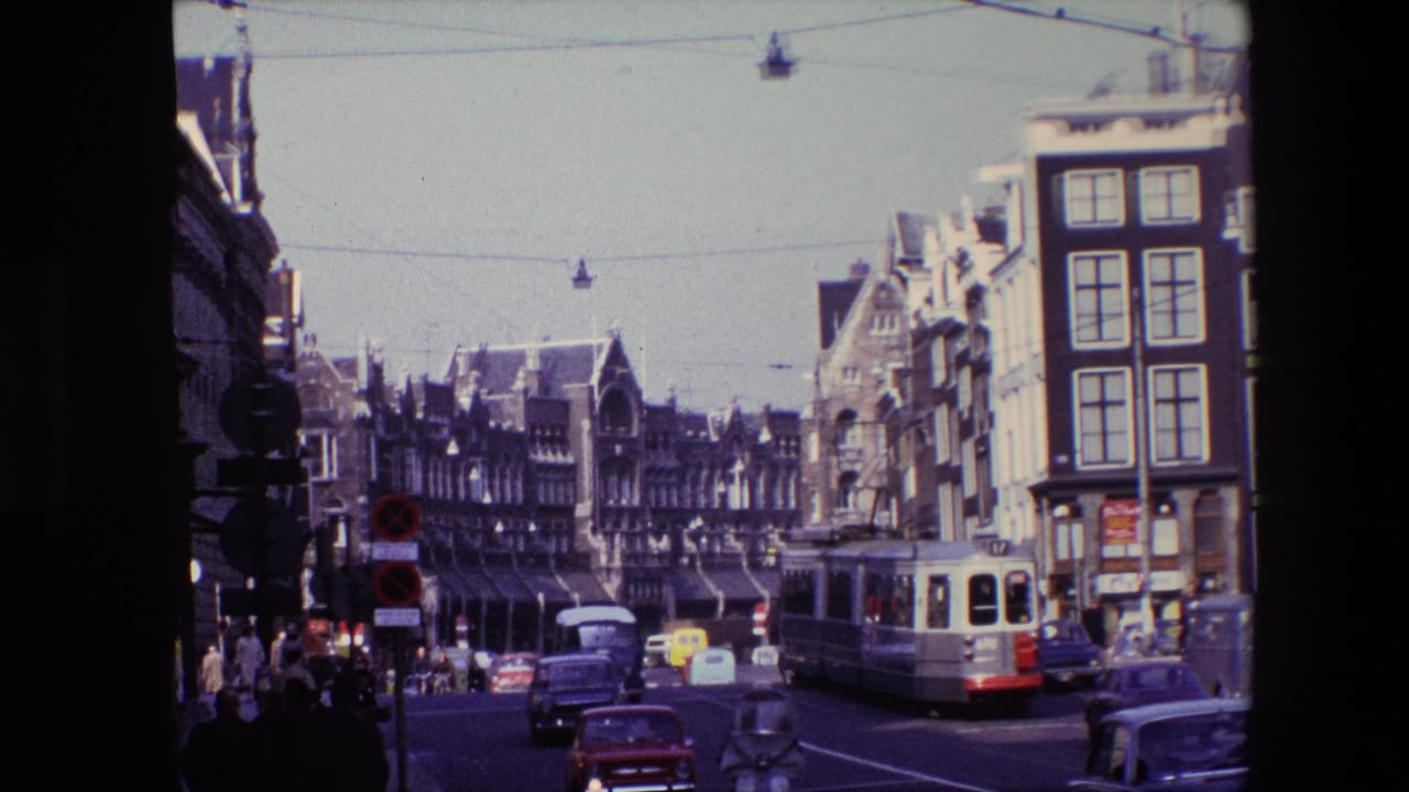 Amsterdam intersection in 1967 with a red-and-white tram, compact cars, cyclists, pedestrians, suspended street lamps, and historic facades.