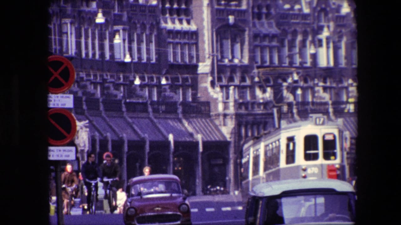1967 Amsterdam street view with cyclists moving through traffic near classic cars, a tram, street signs, and tall historic facades.